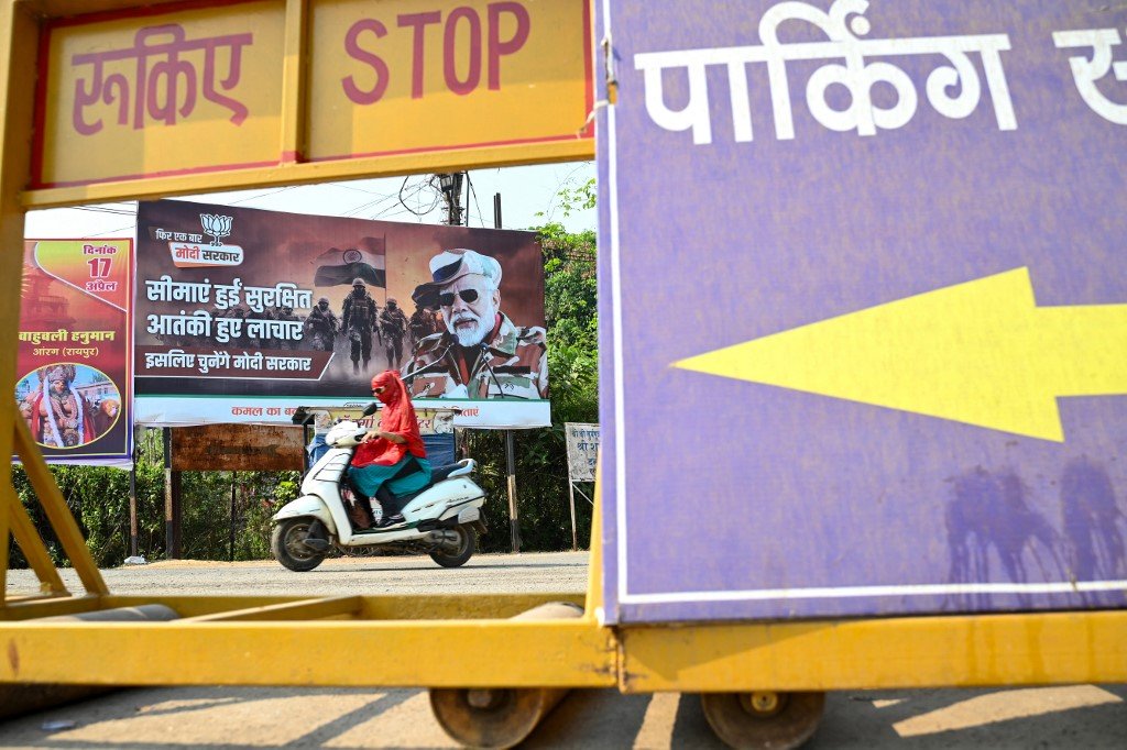 印度全国大选前夕，在恰蒂斯加尔邦丹特瓦达区,一名妇女开车经过印度总理莫迪的竞选海报。（图取自法新社）